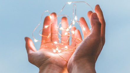 hands holding fairy lights on light blue background