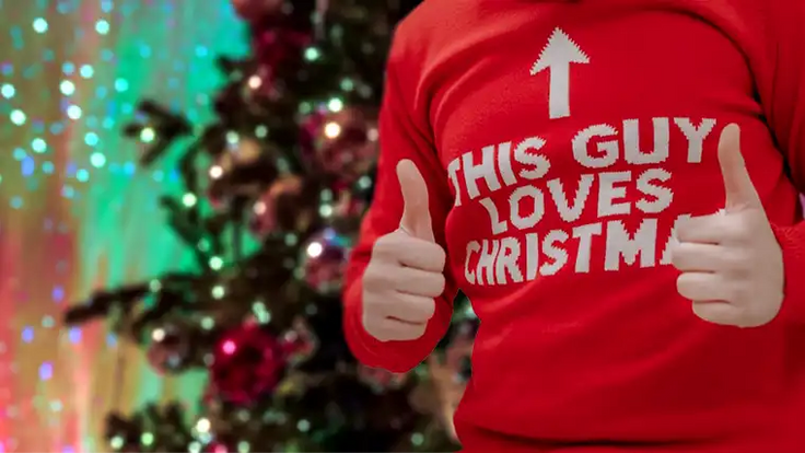 man wearing ugly christmas sweater in front of christmas tree