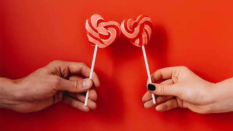 hands holding heart-shaped lollipops on red background 