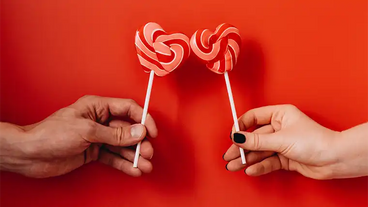 hands holding heart-shaped lollipops on red background