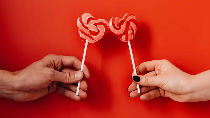 hands holding heart-shaped lollipops on red background