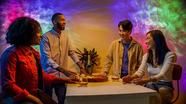 smiling people gathered around table with multicolor galaxy lights