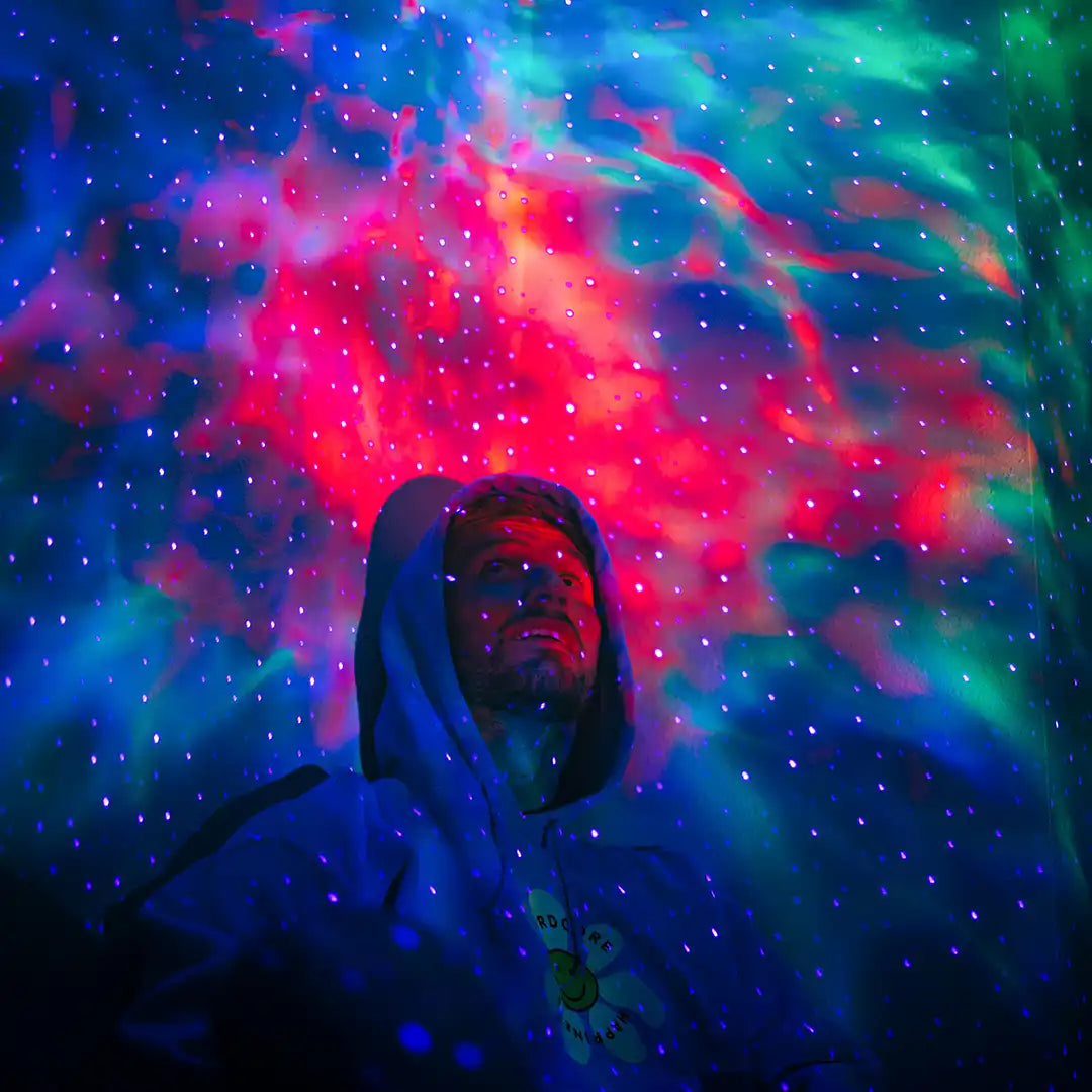 man in hoodie sitting under colorful galaxy lights