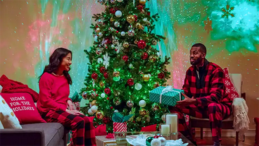 couple opening presents next to christmas tree in living room