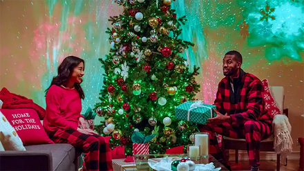 couple opening presents next to christmas tree in living room