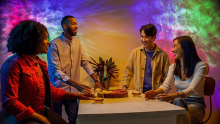 smiling people gathered around table with multicolor galaxy lights