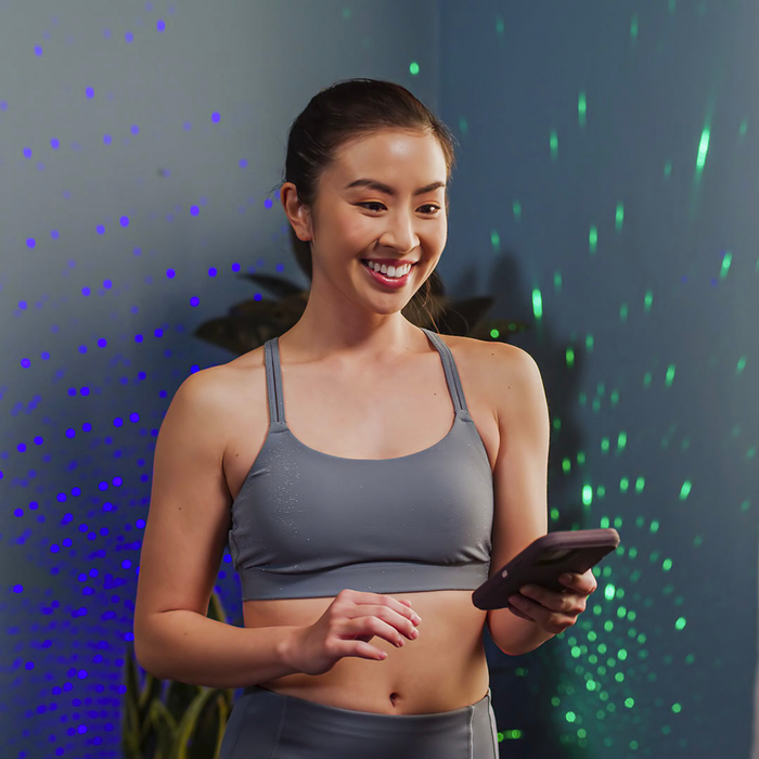 smiling asian woman in workout clothes using app to control lights